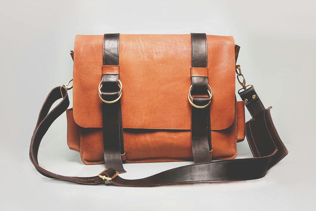 Elegant brown leather briefcase with dark straps and metal buckles, ideal for fashion and business.
